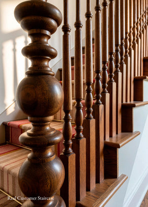 Close-up of a wooden staircase with turned balusters and a striped carpet runner, photographed in a real interior setting.