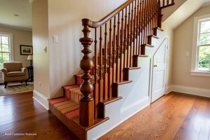 A real residential staircase with a richly carved dark brown wooden banister and handrail, wooden steps, a striped carpet runner, and a white interior door under a slanted ceiling.