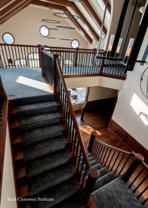A grand interior staircase with dark gray carpeted steps, dark wood railings, and warm wood walls under a high vaulted ceiling with skylights.