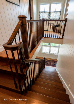 A wooden staircase with dark brown hardwood steps, a matching wooden handrail with spindle balusters, and white paneled walls. 