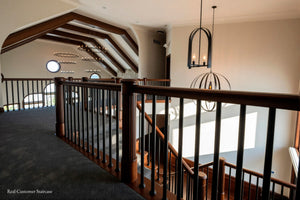 A custom wooden staircase with dark brown wood railings and balusters, carpeted in dark gray, situated on an upper level with a vaulted ceiling and modern chandeliers.