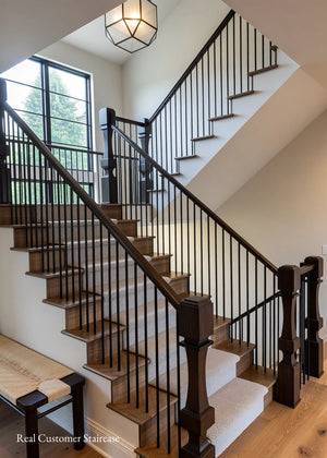 A modern staircase with medium brown wood steps, black metal balusters, and a dark wood handrail in a bright home interior.

