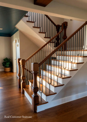 A residential staircase with wooden treads, a dark wood banister, and black metal balusters, shown in a home interior with hardwood floors and a dark blue ceiling.
