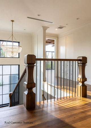 A modern wooden staircase with a dark wood handrail, square turned balusters, and thin black metal vertical balusters, shown in a bright home interior with hardwood floors and a chandelier.