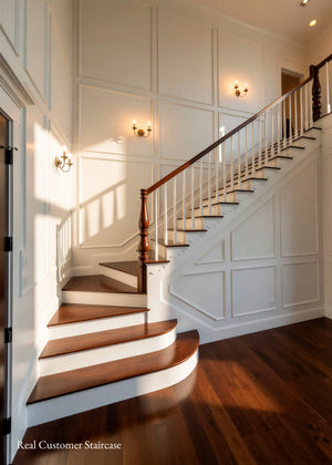 A classic interior staircase with dark brown wooden treads and handrail, white balusters, and white paneled walls with warm wall sconces. A dark hardwood floor is visible in the foreground
