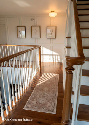 A real residential staircase interior with hardwood flooring, white walls, framed wall art, a long runner rug, and a wooden handrail with white balusters. A small watermark in the lower left reads 'Real Customer Staircase'.