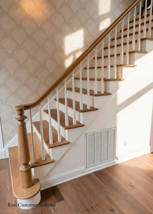 A staged interior staircase with light oak wood treads, white balusters, and a matching wood handrail against a wall with beige patterned wallpaper and hardwood flooring.