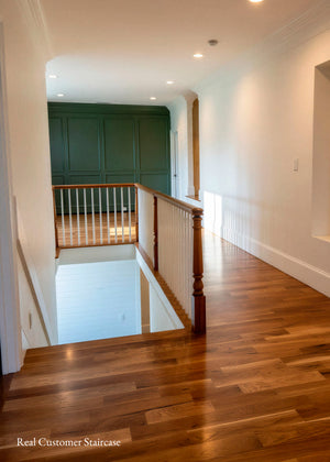 A real staircase interior with hardwood flooring, white walls, a wooden handrail with white balusters, recessed ceiling lights, and a dark green paneled wall at the top. 
