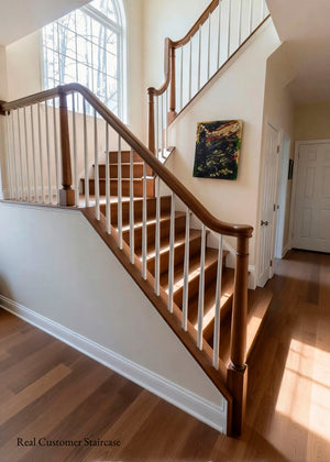A custom wooden staircase with a warm medium-brown wood handrail and spindles, set in a home interior with hardwood floors and cream walls.